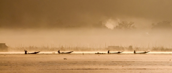 Silhouettes of four fishermen on boats in Myanmar (Burma) go to Inle lake during sunrise with morning fog