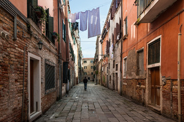 A man walking on an almost empty street under drying bed linens in Venice, Italy