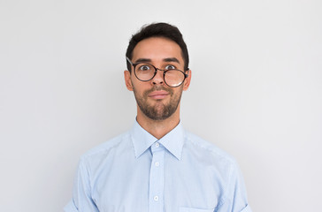 Portrait of frustrated puzzled male with stubble, frowns face, wearing round spectacles posing over white studio background, expresses negative emotion. People, dislike, facial expressions concept