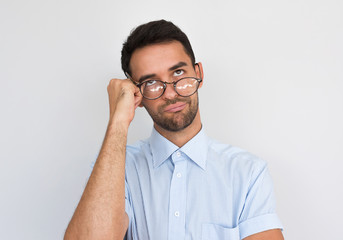 Closeup shot of tired male feels bored, leans on hand, has displeased expression, wearing in casual blue shirt, stands against white studio background. People, facial expressions concept