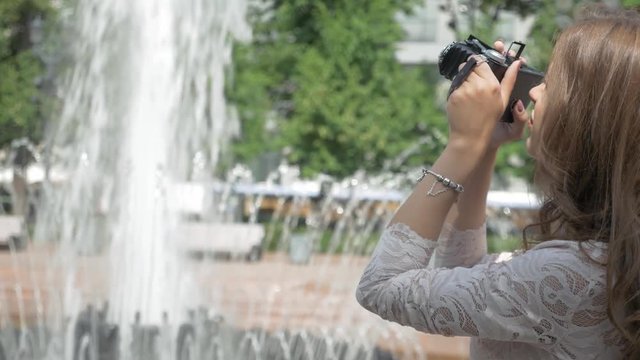 Beautiful girl is taking photos of a city fountain, on a vintage camera