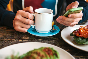 A person in a cafe uses a mobile phone and drinks coffee or tea and has breakfast