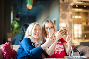 Two young women in a cafe at a table do selfie on phones. Visitors to the restaurant take pictures of themselves on the phone. Focus on phones