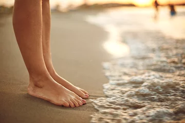 Photo sur Plexiglas Eau Female legs on the beach sand of the sea in summer on vacation.