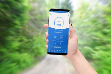 Female runner holding smartphone and checking progress while running in park