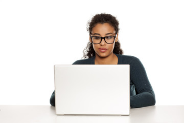 Smiling and positive young african-american woman with beautiful face using laptop computer, working project at desk on white background