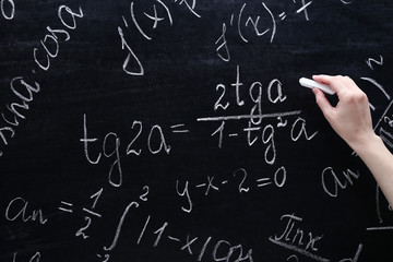 Female hand writing maths formulas on chalkboard