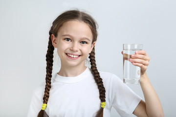 Young girl with glass of water on grey background