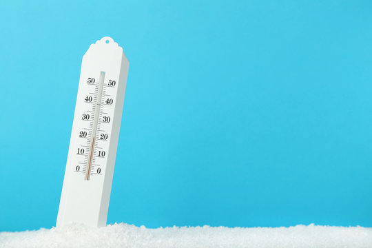 White thermometer in snow on blue background
