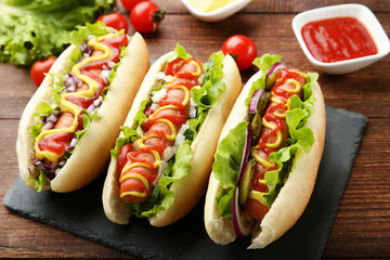 Hot dogs with ketchup, mustard and vegetables on wooden table