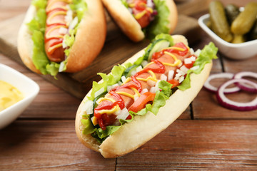 Hot dogs with ketchup, mustard and vegetables on wooden table