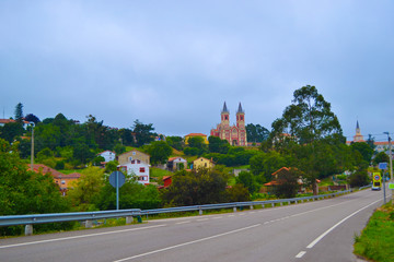 Fototapeta na wymiar Road to Cobreces and San Pedro ad Vincula church (Iglesia de San Pedro ad Vincula) with houses around at the background, in Cobreces, Cantabria, Spain
