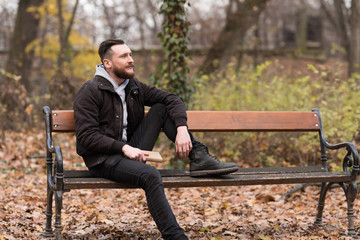 Fototapeta premium A handsome young hipster man sitting on a bench with a book and daydreaming.
