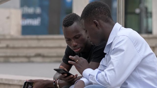 two young black african using smartphone sitting in the city