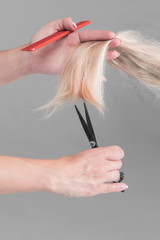 Female hairdresser hold in hand between fingers lock of blonde hair, comb and scissors closeup. Image of hairdresser trimming ends of blonde hair Keratin restoration, latest trend, fresh idea