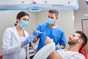 A handsome dentist and a beautiful assistant giving dental treatment to the patient.