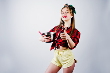 Young funny housewife in checkered shirt and yellow shorts pin up style with saucepan and kitchen...