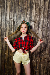Obraz premium Young funny housewife in checkered shirt and yellow shorts pin up style on wooden background.