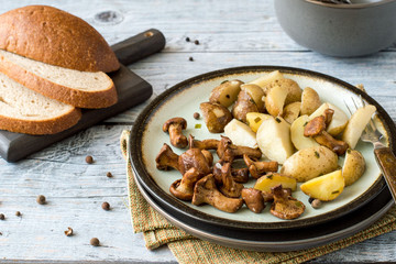 Fried mushrooms chanterelles and young potatoes on a round plate on an old wooden table.