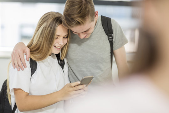 Boy embracing girl in school and looking at cell phone together