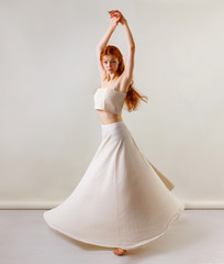 Naklejka premium Dancer posing in studio. Young and beautiful redhead girl in a beige long skirt and top dances and poses in studio. Copy space, gray background