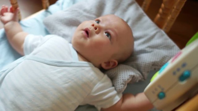 A three-month-old child is very happy with the new toy. The kid laughs, pulls his legs and watches his mobile eyes