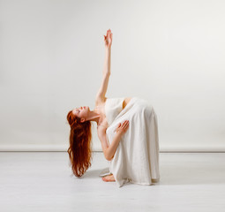 Young redhead woman does stretching and yoga poses, dancing contemporary dance, posing in studio, . Copy space