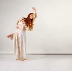 Obraz premium Dancer posing in studio. Young and beautiful redhead girl in a beige long skirt and top dances and poses in studio. Copy space