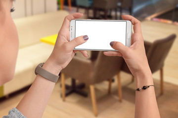 Woman's hands holding smartphone with empty screen in horizontal position , blurred cafe in background