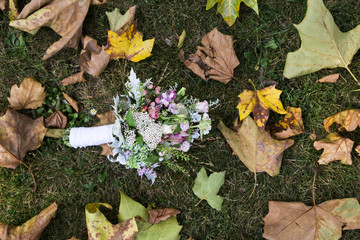 Bouquet of orchids and roses lying on grass near maple leaves