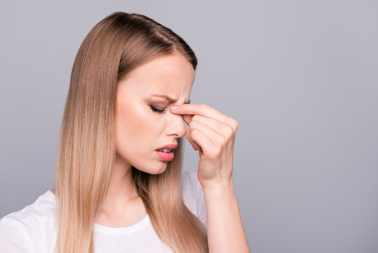Close up portrait of exhausted young woman, holding her nose bridge with closed eyes, she is tired and depressed isolated on gray background