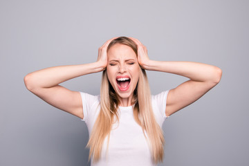 Fototapeta premium Portrait of young blonde attractive gorgeous caucasian charming girl overreacting screaming loudly touching head with hands. Isolated over grey background