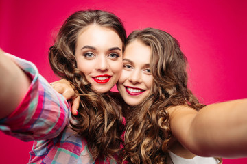 Close-up of adorable sisters or best friends making self-portrait with camera over red background.