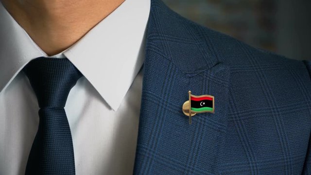 Businessman Walking Towards Camera With Country Flag Pin - Libya