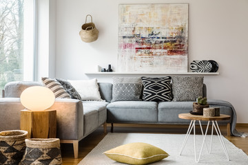 Yellow pillow and table on carpet in bright living room interior with light next to couch. Real photo