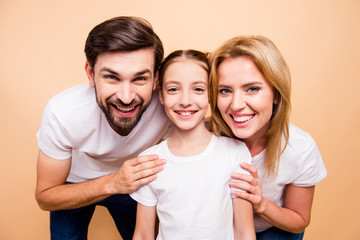 Cheerful attractive smiling bearded father and blonde mother hugging their little daughter on beige background