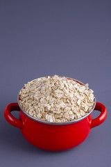 Red pan with dry oat flakes on gray background. Closeup. Concept healthy eating