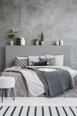 Front view of a comfortable bed with linen, pillows, a blanket and an open book on it in a grey...