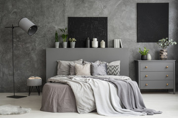 Ash grey bedroom interior with two black paintings on the wall above a bed with bedding and...