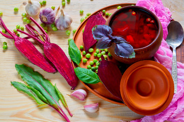 Homemade borscht with vegetables on the wooden background with fresh sliced beet, garlic, basil leaves and green peas. Traditional Ukrainian, Polish and Russian national beetrot soup. Top view