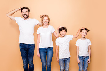 Portrait of young beautiful family, bearded father, blonde mother and their little children wearing jeans and white T-shirts, standing in order of hierarchy, placing hands of heads of each other