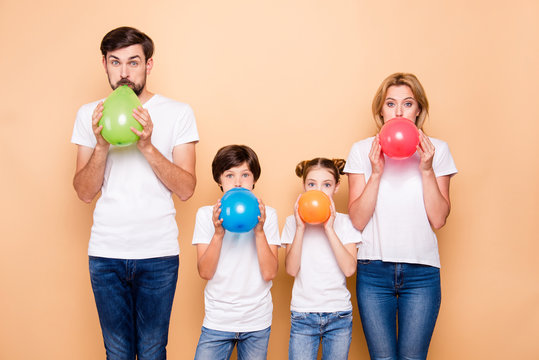 Young family, bearded father, blonde mother, boy and girl wearing blue jeans and white T-shirts, blowing air balls green beige red blue