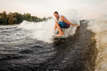 Happy young wakesurfer riding down the river on board