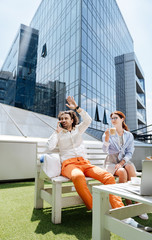 Waving friend. Rich stylish businessman wearing white shirt and orange trousers waving his friend sitting in cafe