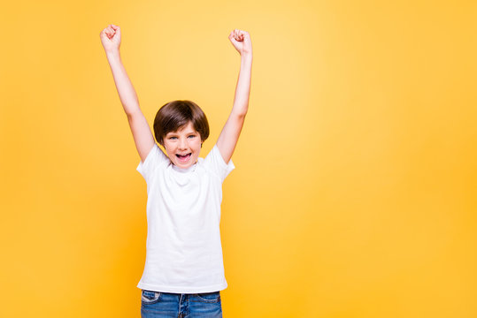 Portrait of attractive young cheerful school boy, smiling raising hands up over yellow background, isolated. Copy space