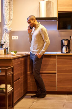 A happy handsome young man talking on his phone and cooking in the kitchen.