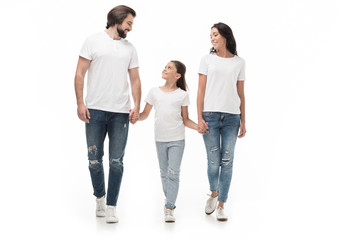 Obraz premium smiling family in white shirts and jeans holding hands while walking together isolated on white