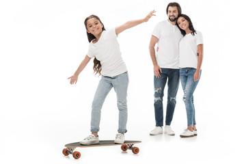 Fototapeta premium smiling parents looking at daughter skating on skateboard isolated on white