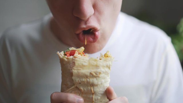 Young man, student sitting at home eating fast food. Shawarma, Shawarma, Shawarma. Healthy or unhealthy fresh food.
