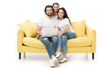 smiling family with laptop sitting on yellow sofa isolated on white